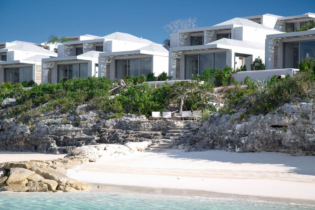 Un hotel costero con varias edificaciones blancas, una playa de arena y terreno rocoso.