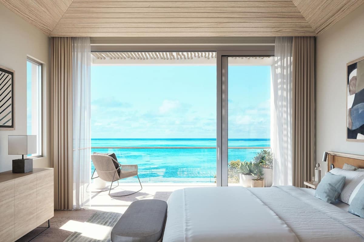 Un dormitorio con una cama grande, una silla, un escritorio y vista al océano.