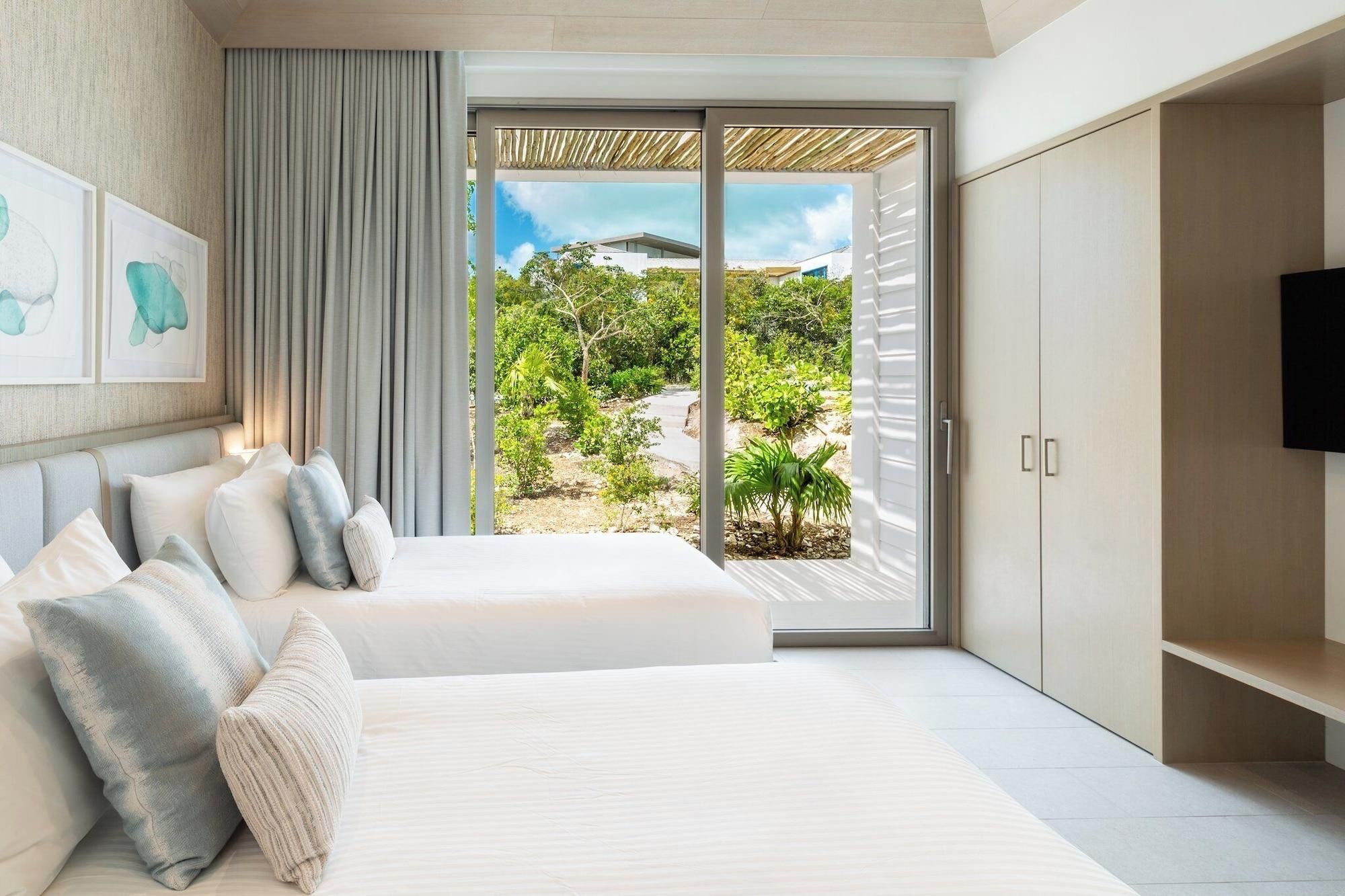 A bedroom with a large bed, a TV, and a sliding glass door leading to a garden.