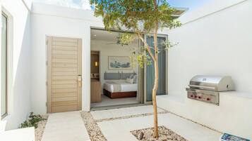 A modern hotel room with a wooden door, a bed, a bathroom, and a barbecue grill.
