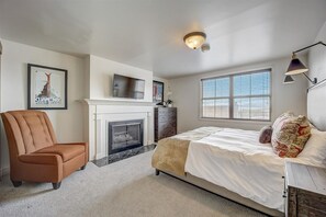 Un dormitorio con cama, una silla, chimenea, televisor y ventana.