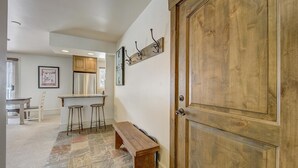 Un pasillo con puerta de madera, un banco y una zona de bar con taburetes.