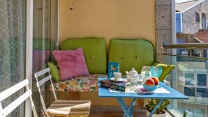 Un balcon avec une table, deux chaises, un canapé vert et diverses plantes.