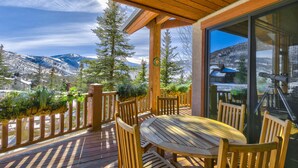 A wooden deck with a table and chairs, overlooking a snowy mountain landscape.