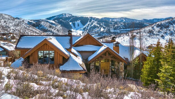 A wooden lodge with multiple gabled roofs, surrounded by snow-covered mountains and clear skies.