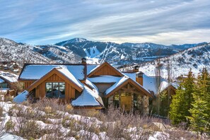 A wooden lodge with multiple gabled roofs, surrounded by snow-covered mountains and clear skies.