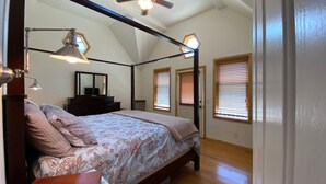 A bedroom with a bed, a dresser, a mirror, and two windows with blinds.