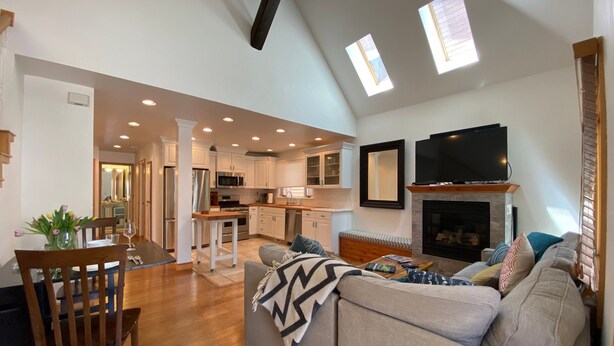 A spacious living area with a sofa, a dining table with chairs, a kitchen area, and a fireplace.