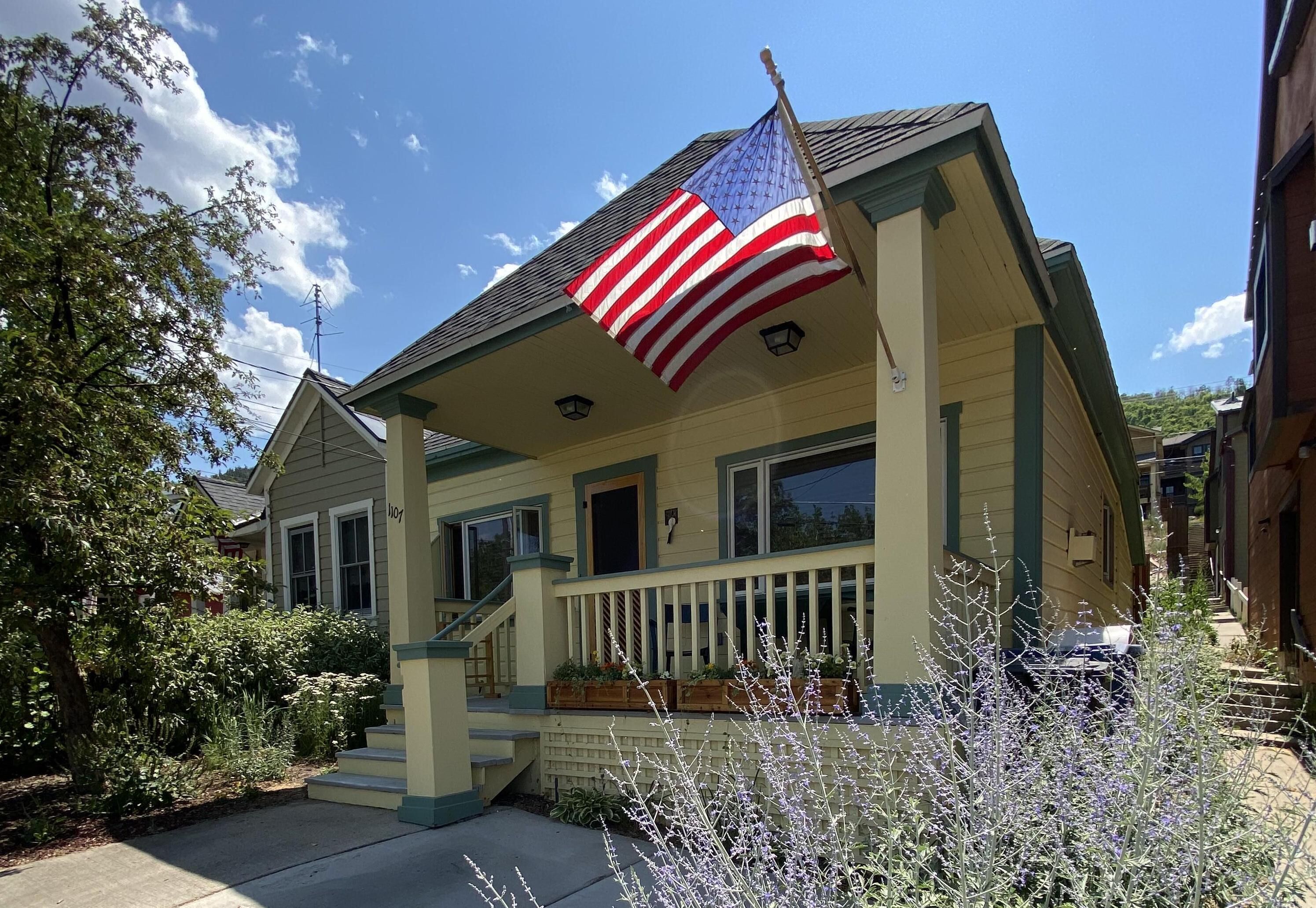 A two-story house with a porch, a flag, and a well-maintained garden.