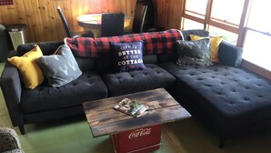 En hyggelig stue med en hjørnesofa, et træbord og et rødt Coca-Cola køleskab.