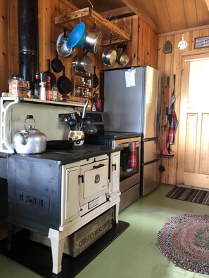 Una cocina con estufa antigua, refrigerador y diferentes utensilios de cocina.