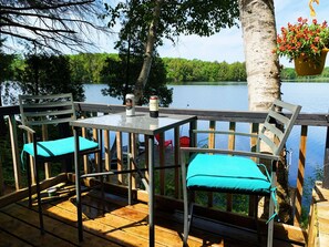Eine Holzterrasse mit zwei Stühlen und einem Tisch mit Blick auf einen See.