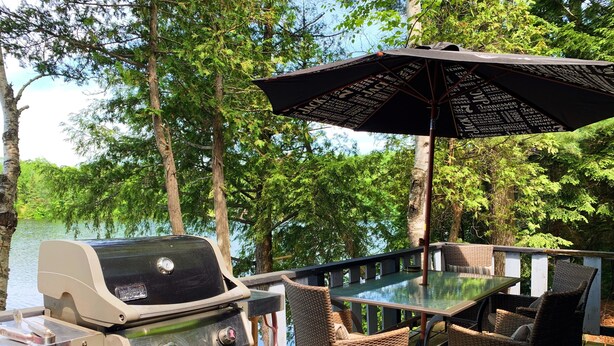 En udendørs terrasse med grill, fletstole og et bord med parasol.