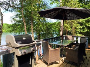Eine Terrasse im Freien mit Grill, Korbstühlen und einem Tisch mit Sonnenschirm.