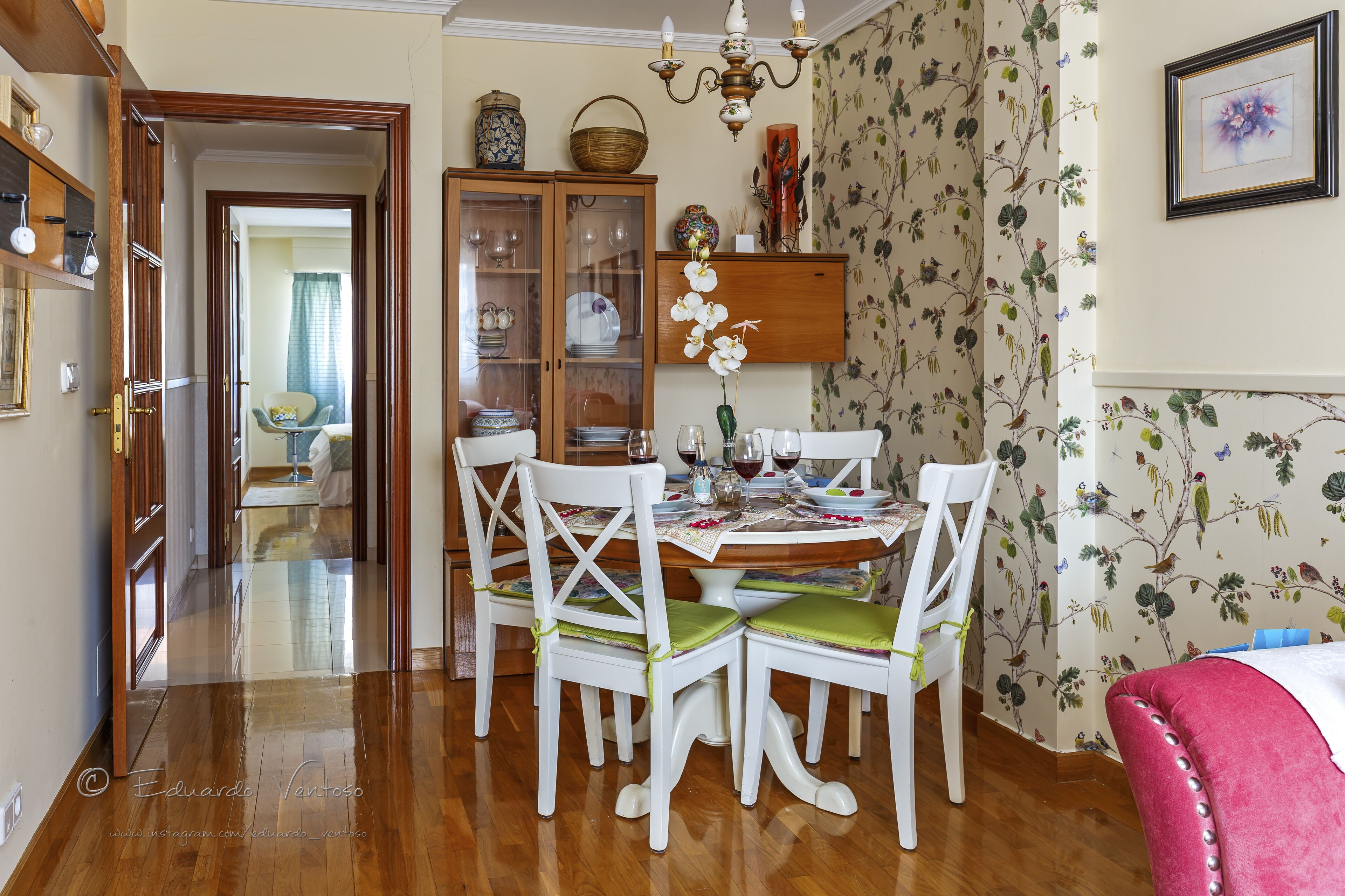 A dining area with a wooden table, white chairs, and a floral wallpaper.