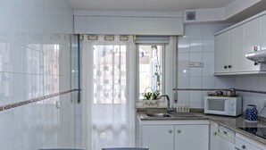 A compact kitchen with white cabinets, a built-in microwave, a sink, and a window with a view of buildings outside. - Noia Compostella Wifi (Noia)
