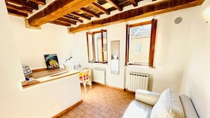 A cozy living area with a sofa, a small table, and a chair. There are windows with wooden frames, a radiator, and a picture frame on the wall. - GuestHost - Cozy 65 sqm apartment, able to accommodate 4 people, located on the 1st floor of a typical medieval building (NO lift). The property is located a short distance from the historic center of Perugia, in the characteristic Sant’Angelo district (Perugia)