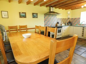 A wooden dining table with chairs, a kitchen with white cabinets, a tiled backsplash, and a stove.
