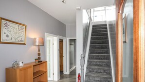 Een trap met een brandblusser, een houten console tafel met een lamp en een lijst met een kaart aan de muur.