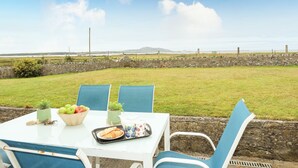 Een terras met eethoek voor twee personen, uitzicht op de zee en een stenen muur op de achtergrond.