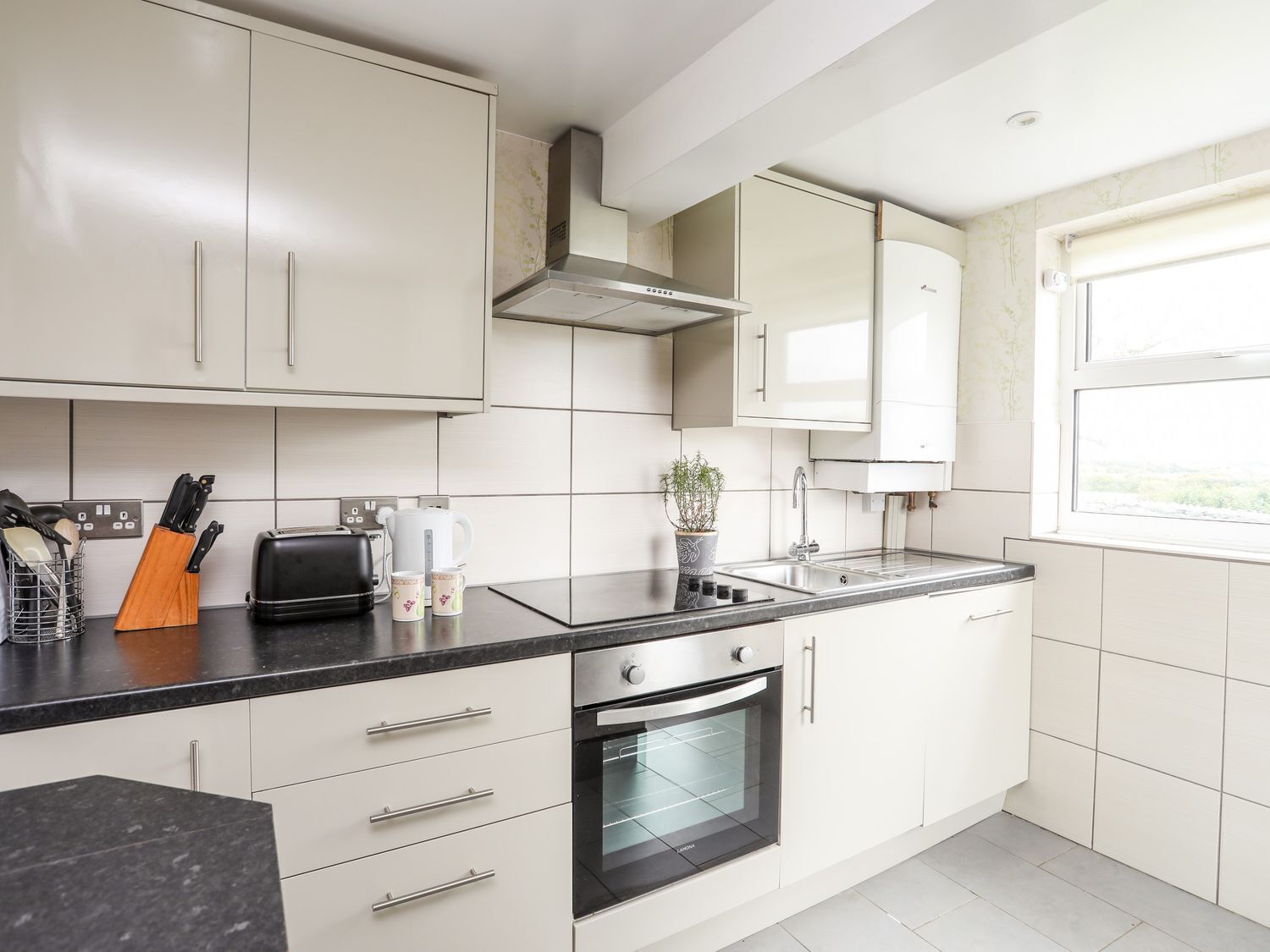 A modern kitchen with white cabinets, a black countertop, a built-in oven, and a window providing natural light.
