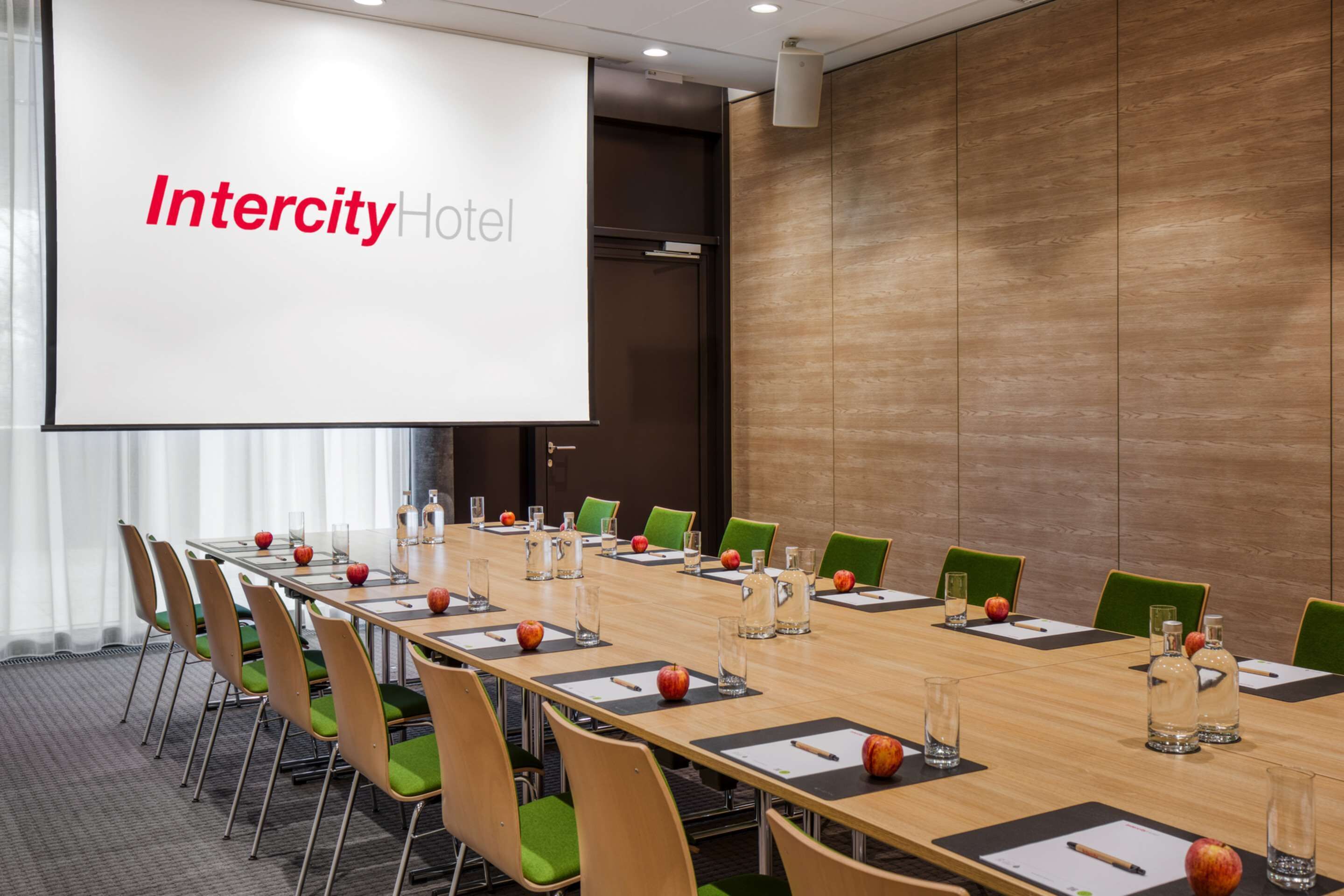 A conference room at Intercity Hotel with a long table, green chairs, and a projector screen displaying the hotel name.