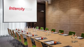 A conference room at Intercity Hotel with a long table, green chairs, and a projector screen displaying the hotel name.