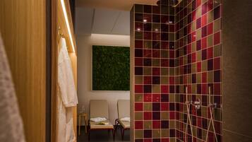A modern bathroom with a shower, two chairs, a towel rack, and a green wall.