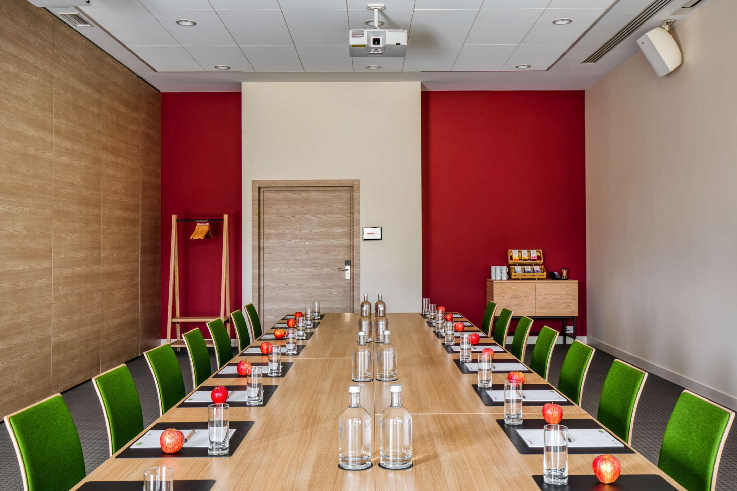 Une salle de conférence avec une longue table, des chaises vertes et des murs rouges.