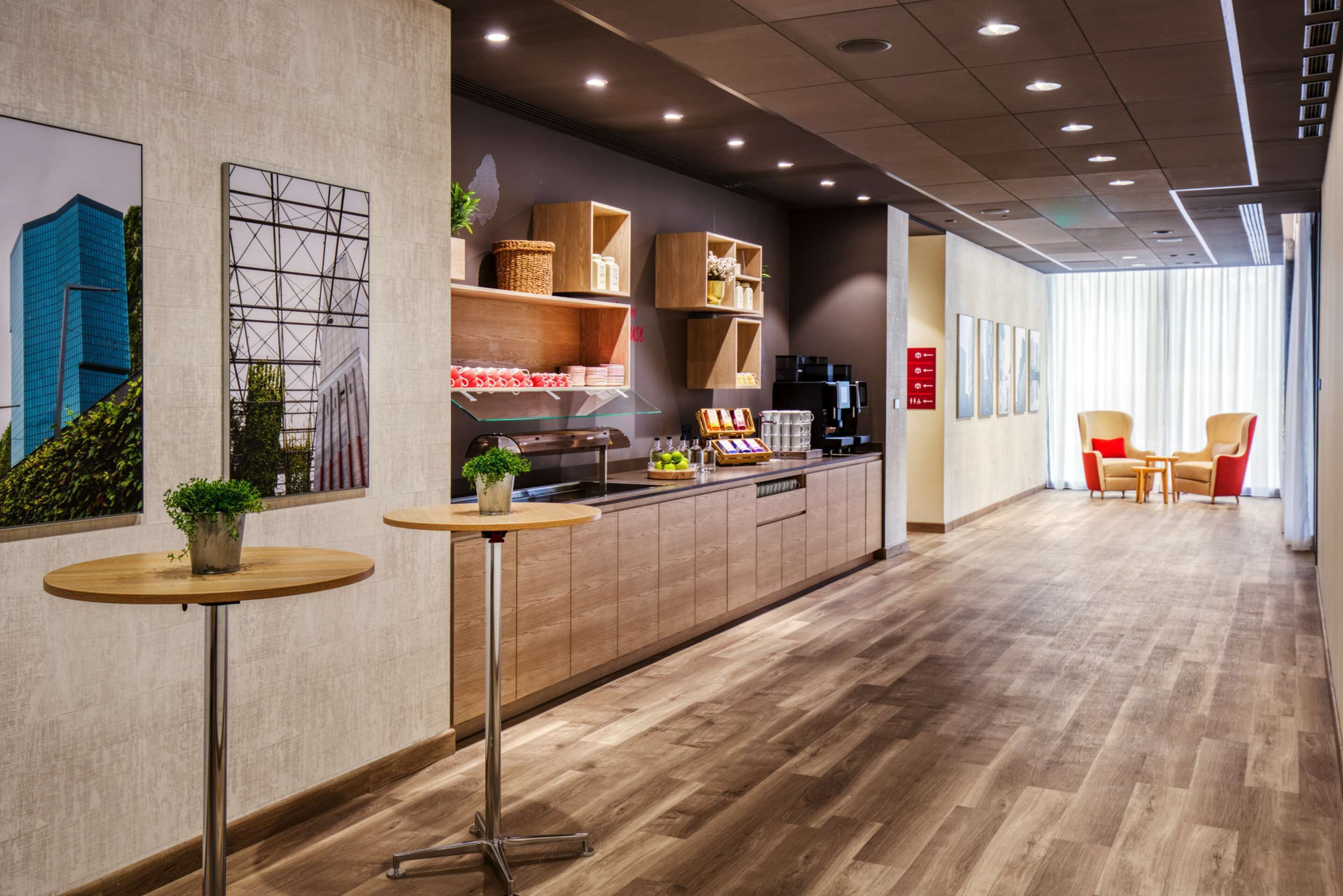 A modern hotel lobby with a wooden reception desk, a coffee machine, and a seating area with chairs.