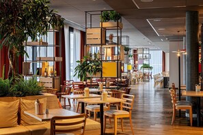 Un restaurante espacioso con mesas y sillas de madera, un arreglo floral central y amplios ventanales que dejan entrar la luz natural.