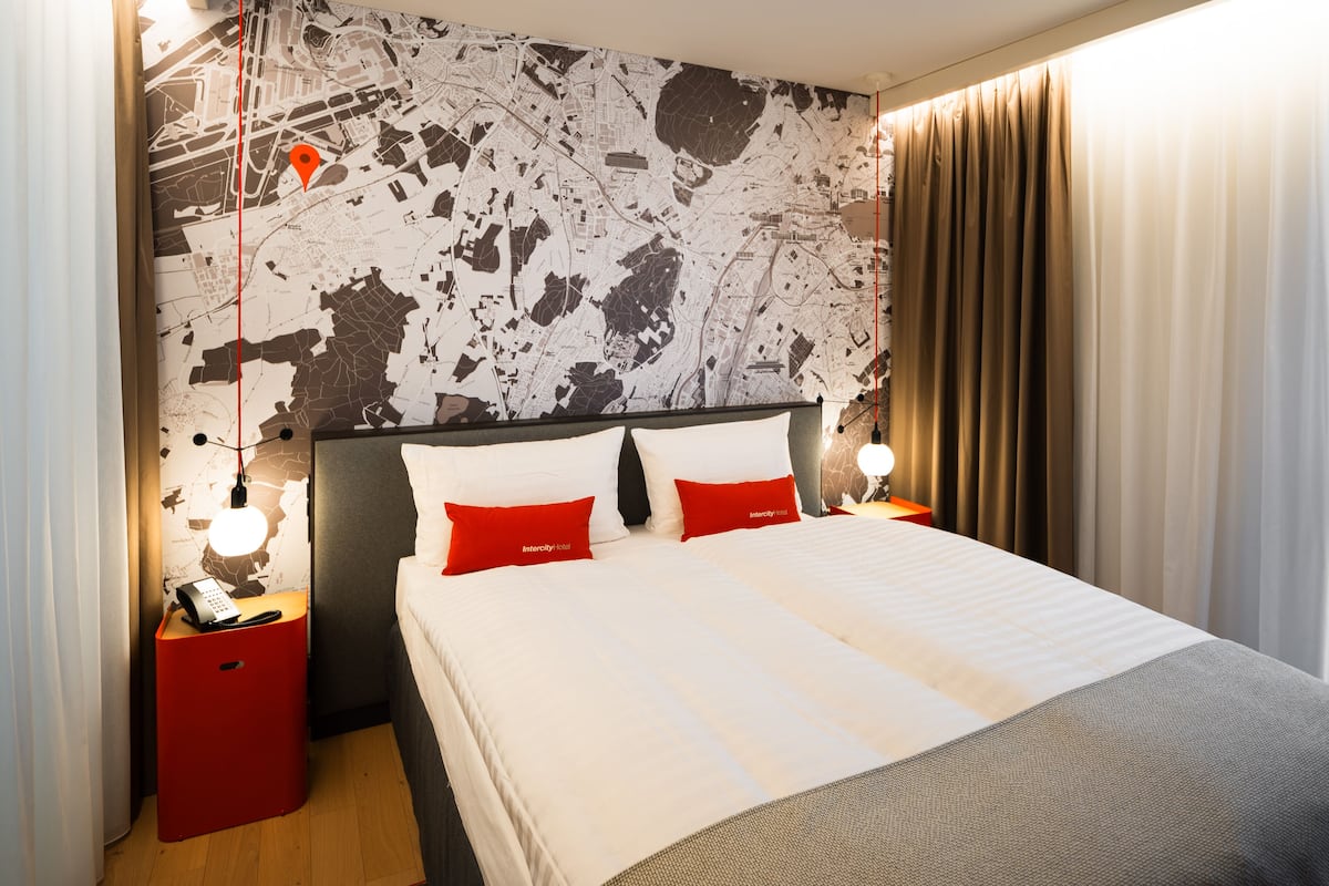 Una habitación de hotel con una cama grande, dos almohadas rojas, una mesita de noche con teléfono y un mapa en la pared.