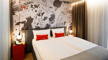 A hotel room with a large bed, two red pillows, a nightstand with a phone, and a map on the wall.