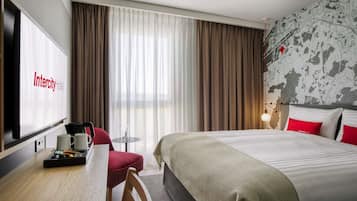 Ein Hotelzimmer mit Bett, Schreibtisch mit Kaffeemaschine, Stuhl und einem Fernseher, der den Namen des Hotels anzeigt.