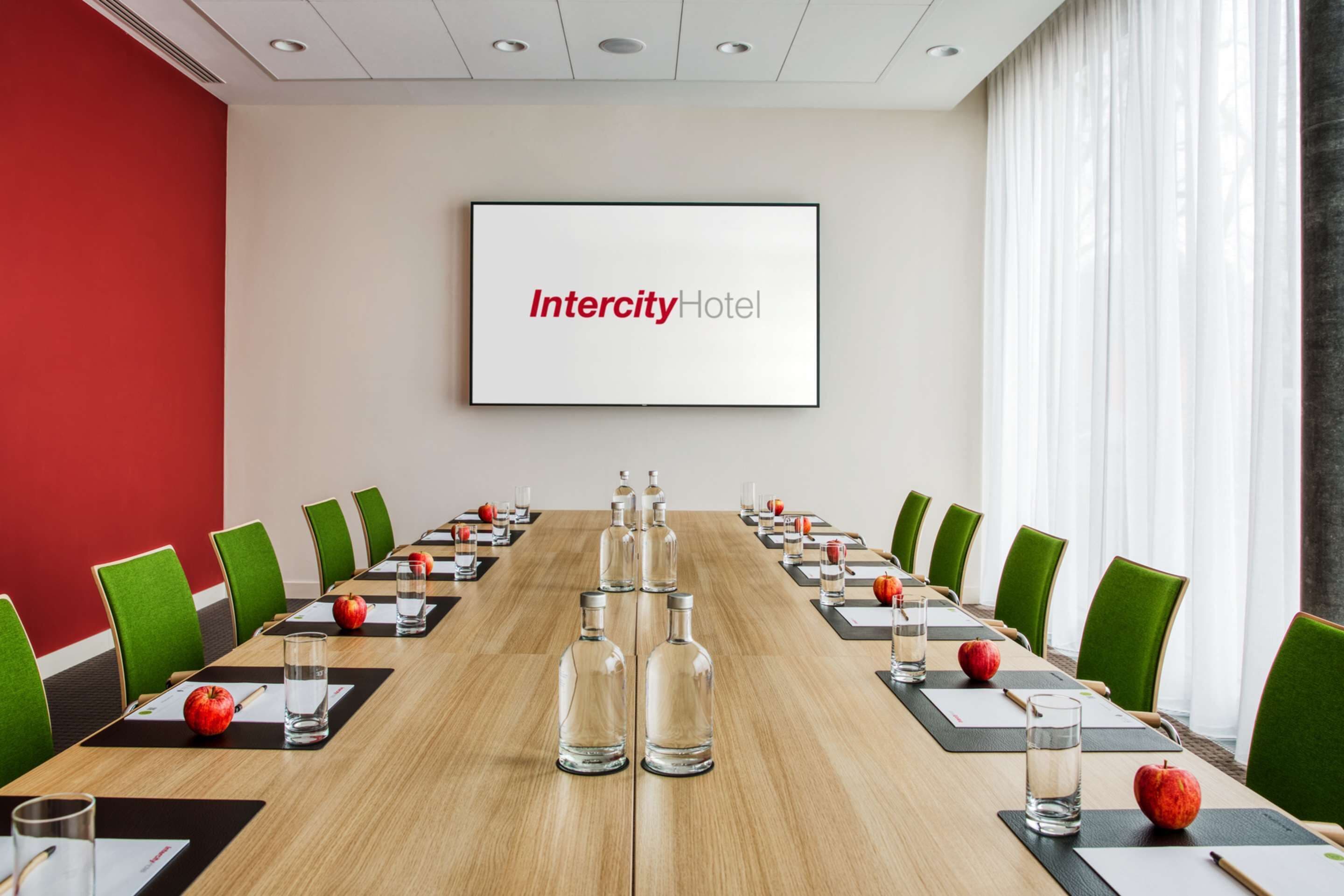 A conference room with a long table, green chairs, and a screen displaying "Intercity Hotel".