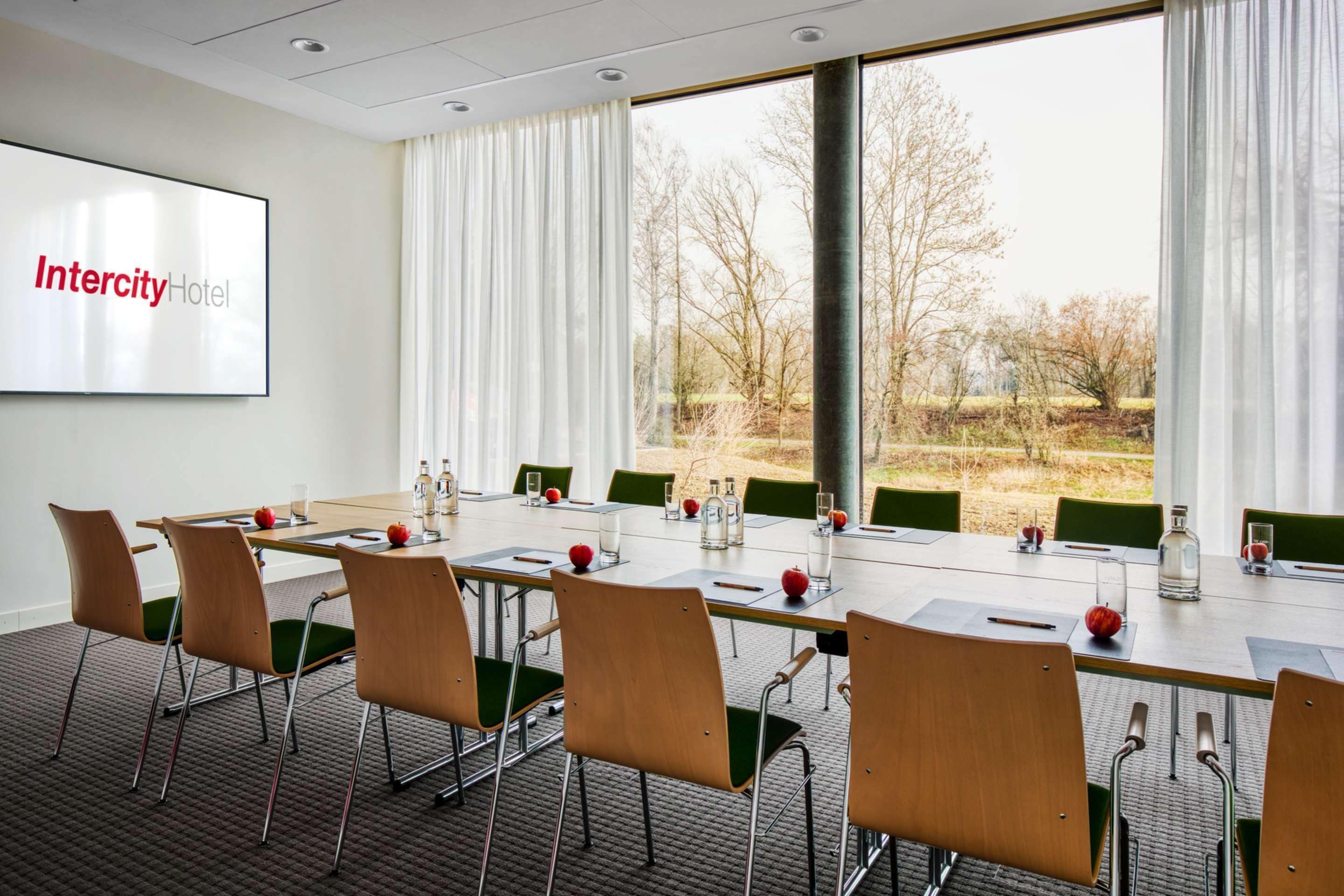 Un salón de conferencias en el Hotel Intercity con una pantalla grande, una mesa larga y sillas verdes.