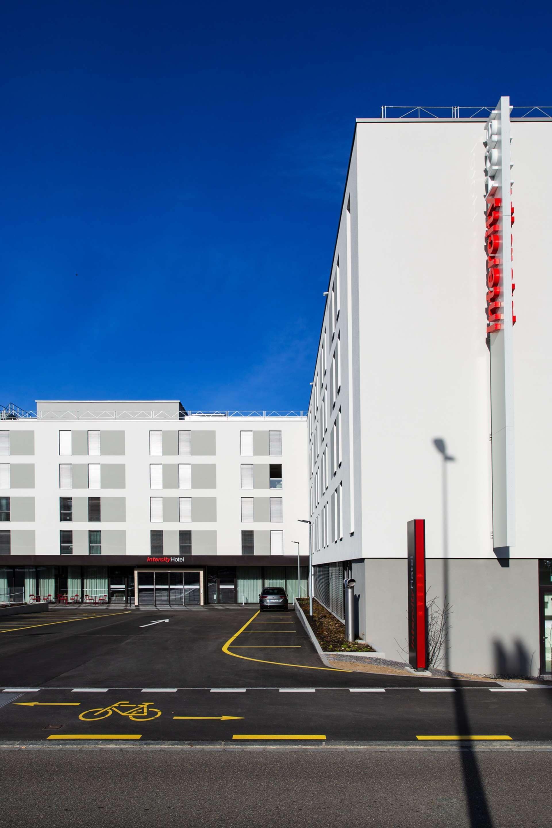 A modern building with a white facade, a clear blue sky, and a bicycle lane leading to the entrance.
