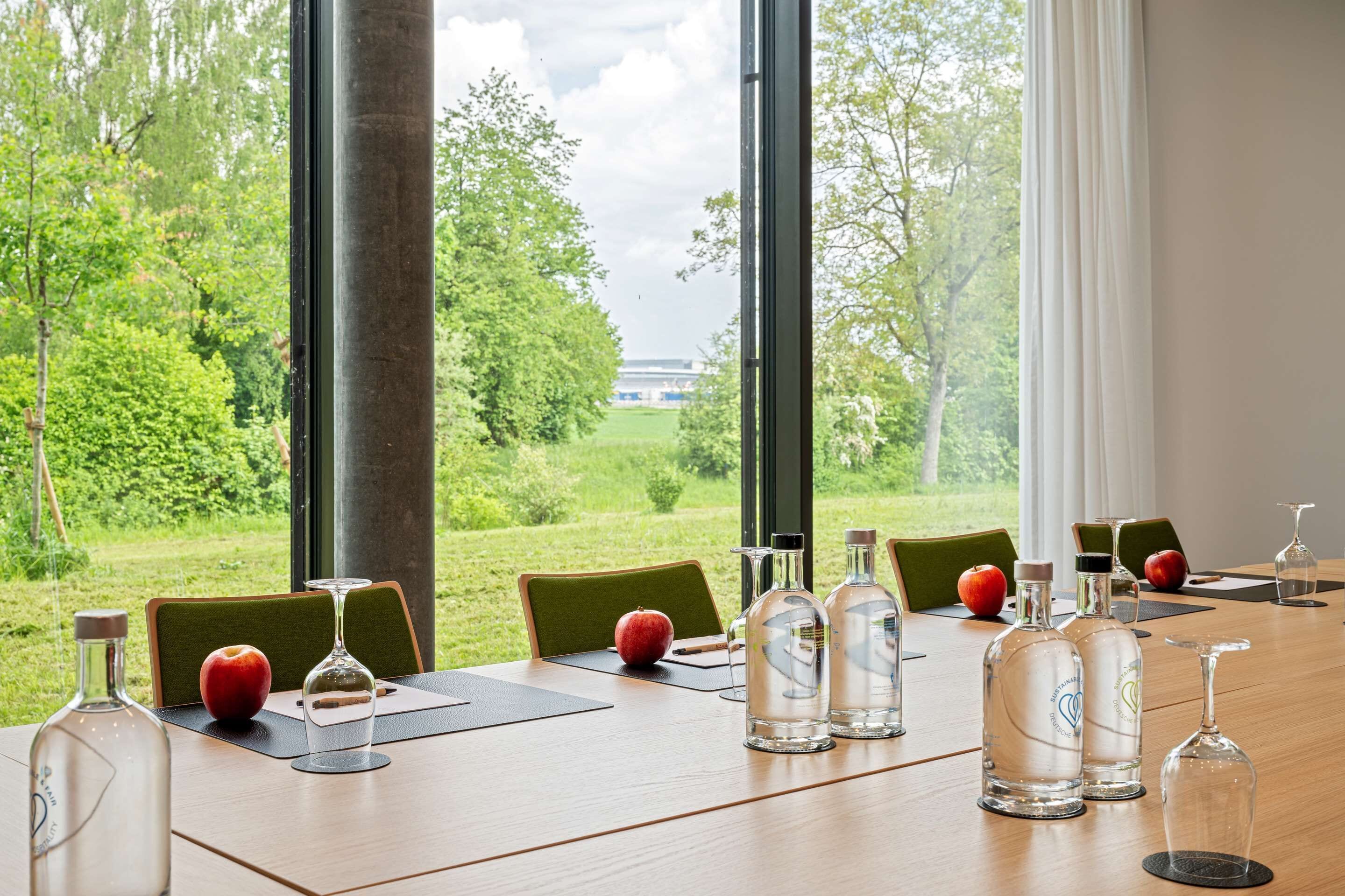 Ein Konferenztisch mit Stühlen, einer Flasche, einem Glas und einem Apfel.