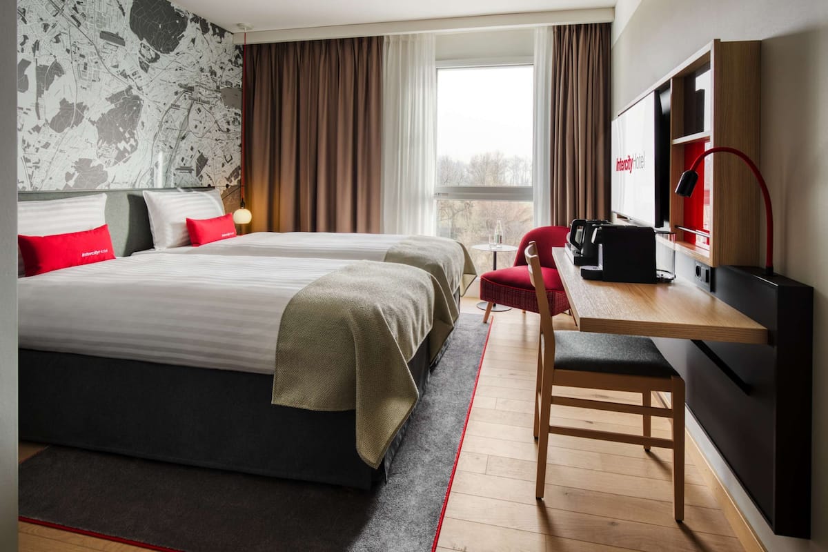 Habitación de hotel con una cama grande, un escritorio con silla, televisor y ventana con cortinas.