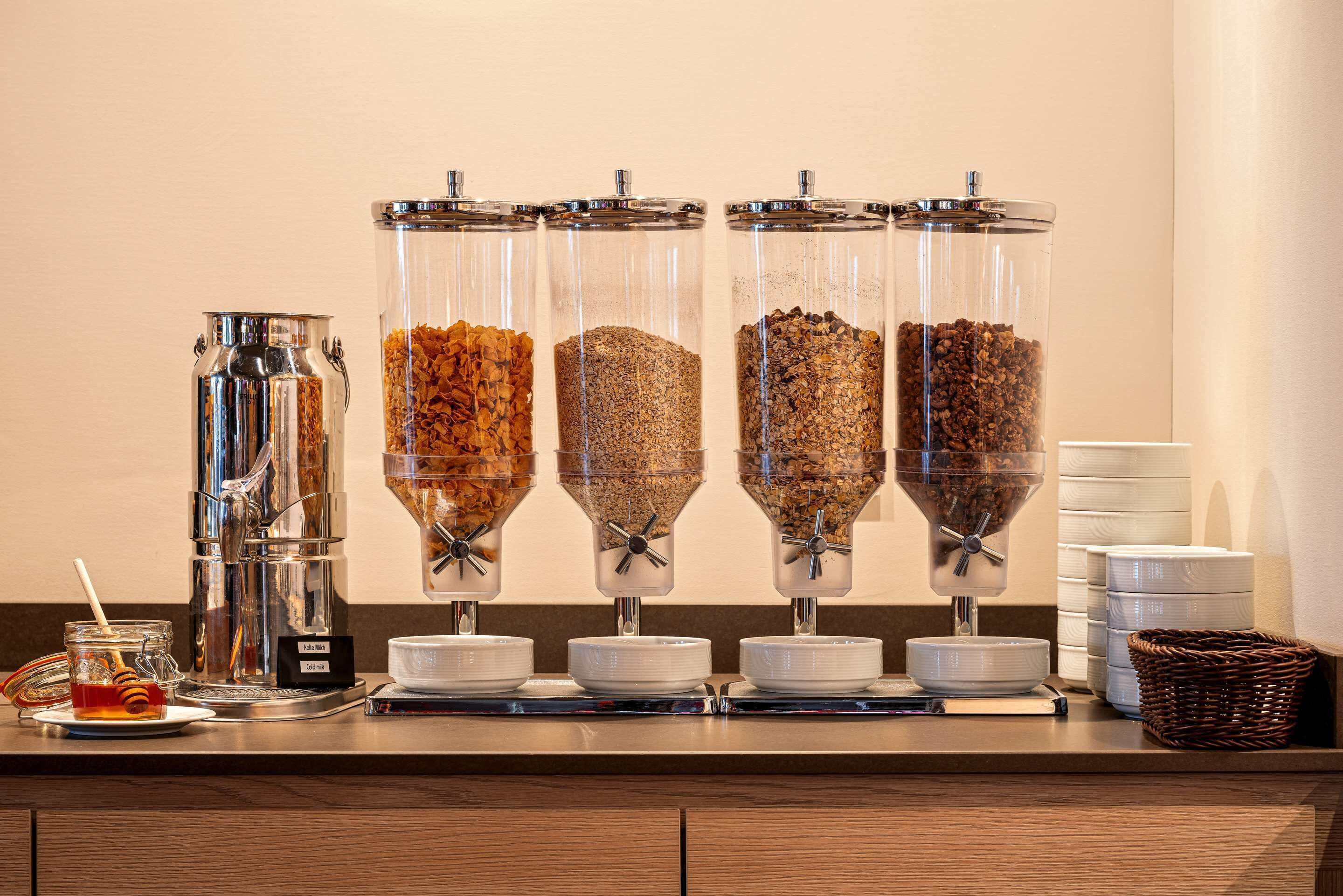 Ein Frühstücksbuffet mit fünf Speiserausgaben, einer Kaffeemaschine und einem Honigglas.
