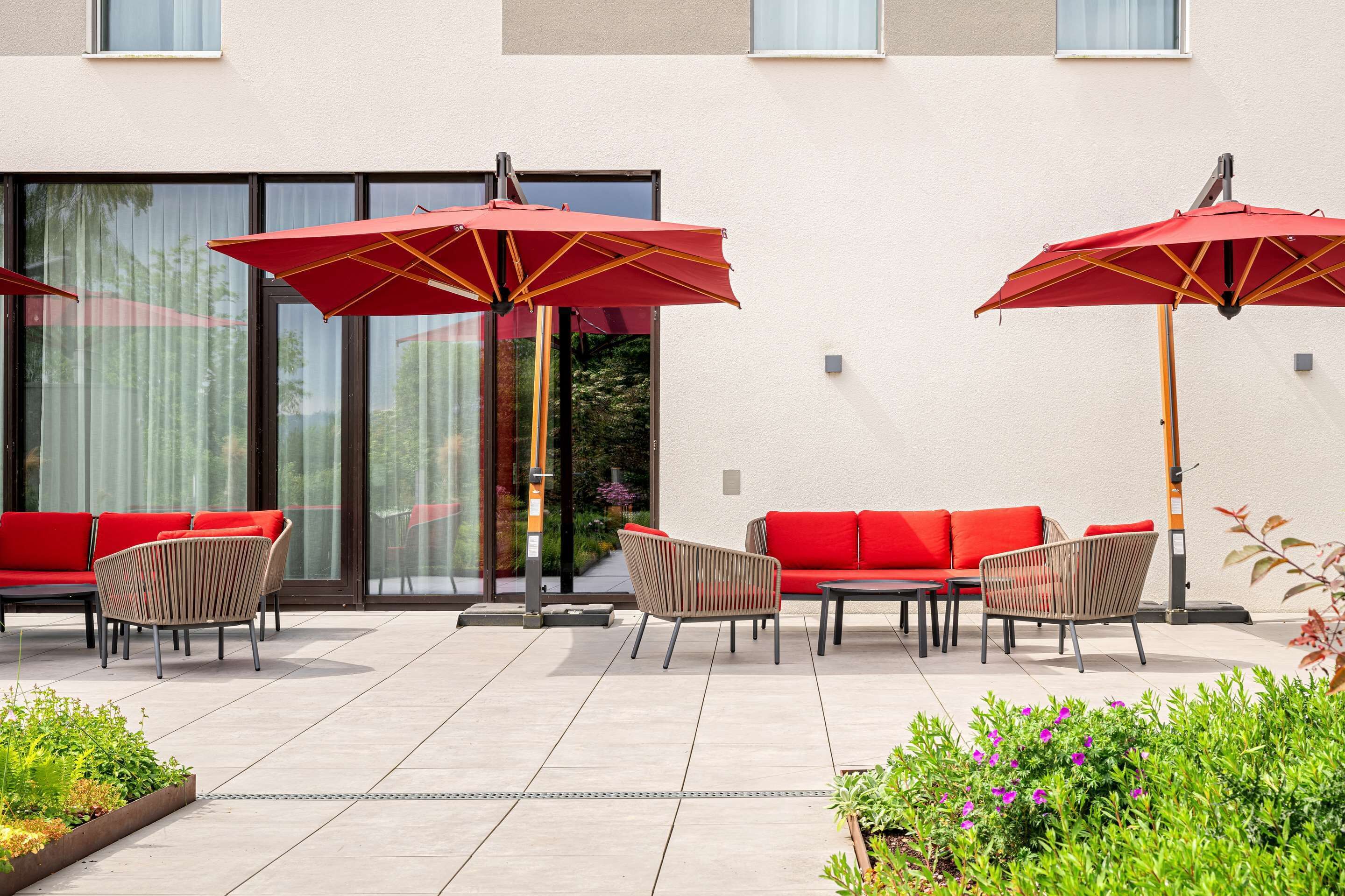An outdoor seating area with red chairs and umbrellas, a red sofa, and a tiled floor.