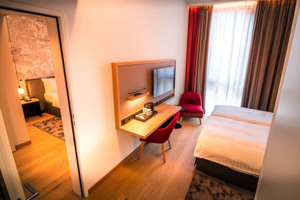 Una habitación de hotel con cama, escritorio, televisor, una silla roja y un mapa en la pared.