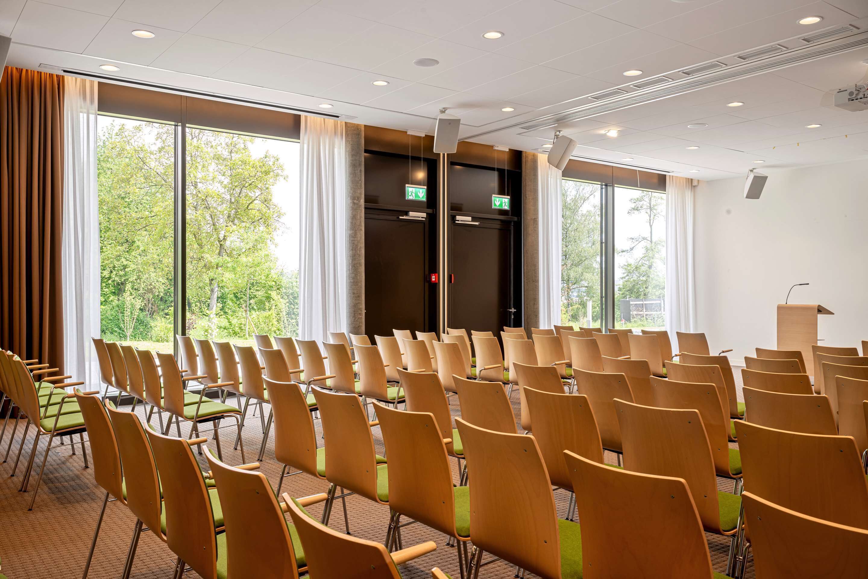 Ein Konferenzraum mit Reihen von Stühlen, großen Fenstern und einer Ausgangstür.