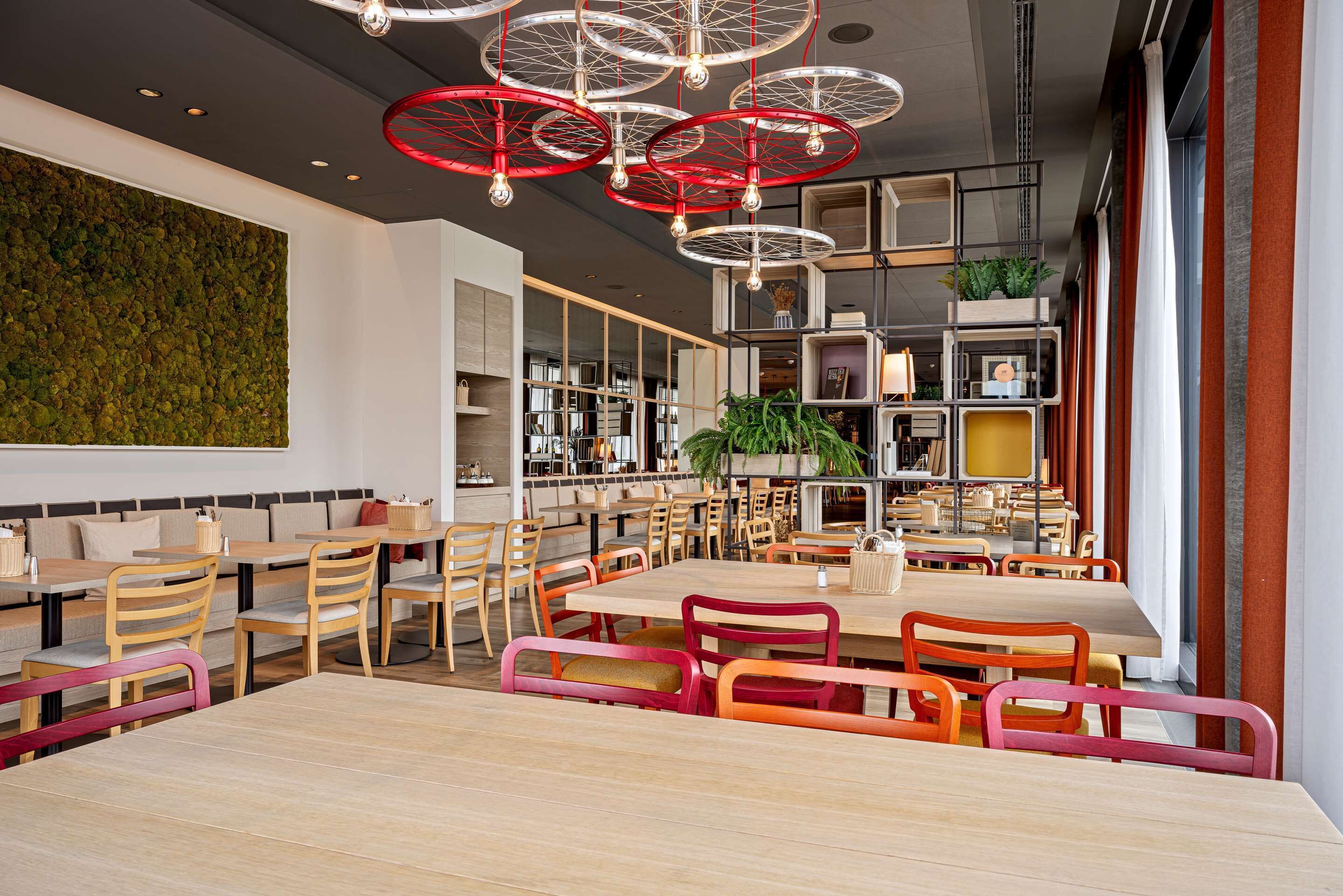 Un restaurante moderno con mesas y sillas de madera, una pared verde y luces colgantes rojas.