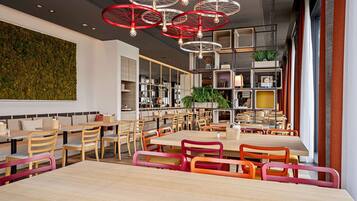 Un restaurante moderno con mesas y sillas de madera, una pared verde y luces colgantes rojas.
