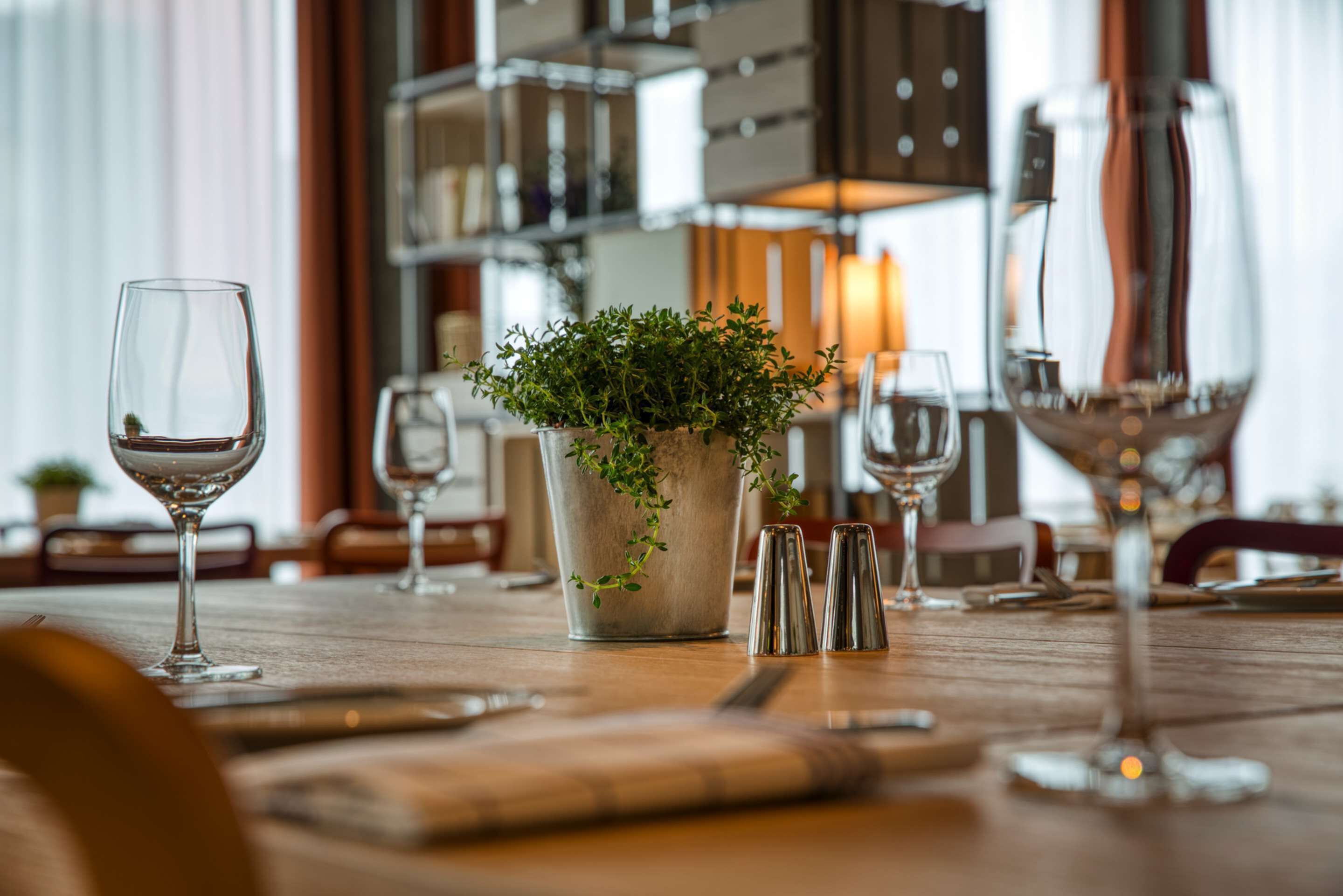 Una mesa de comedor con copas de vino, una planta en maceta y saleros y pimenteros.