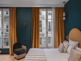 Ein Hotelzimmer mit Bett, Sessel und großen Fenstern mit Vorhängen.
