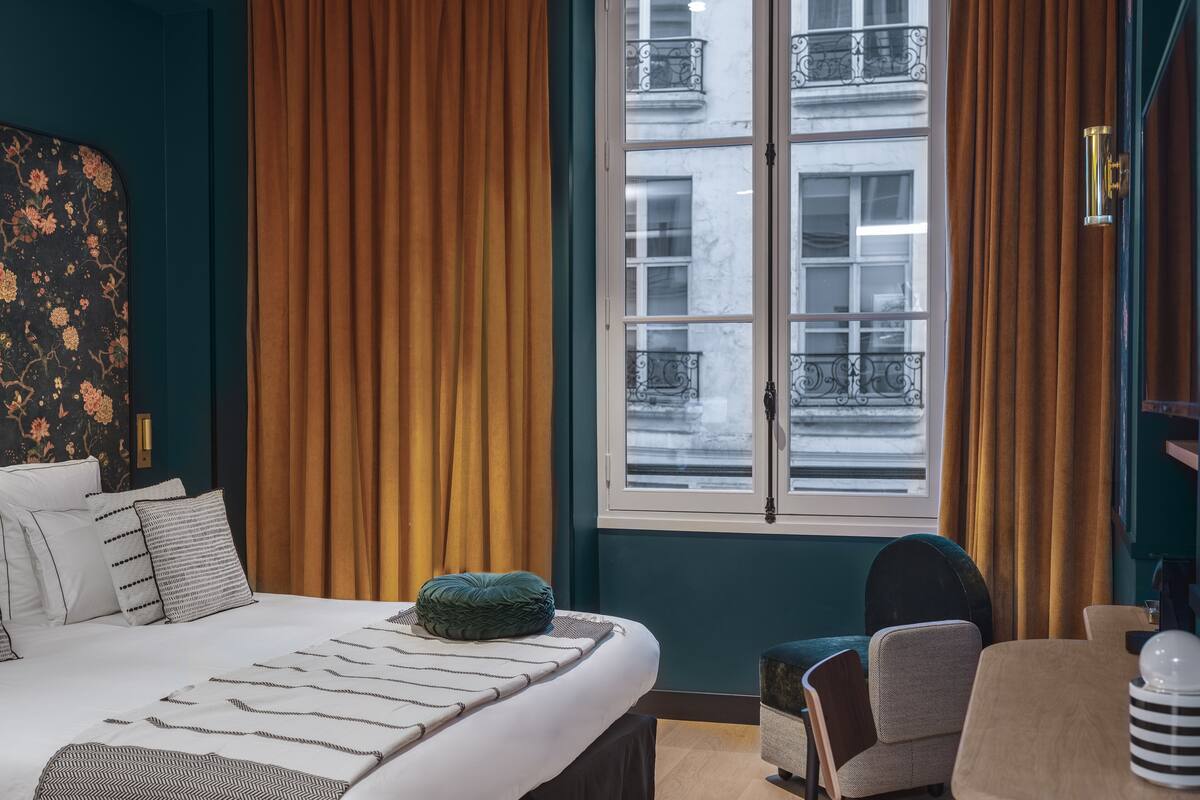 A hotel room with a bed, a chair, a table, and a window with curtains.