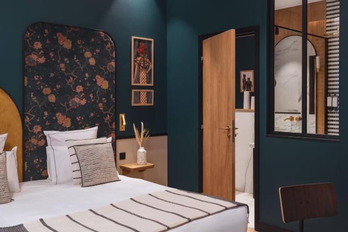 A bedroom with a floral headboard, a bed with striped bedding, a nightstand with a vase, and a wooden door.