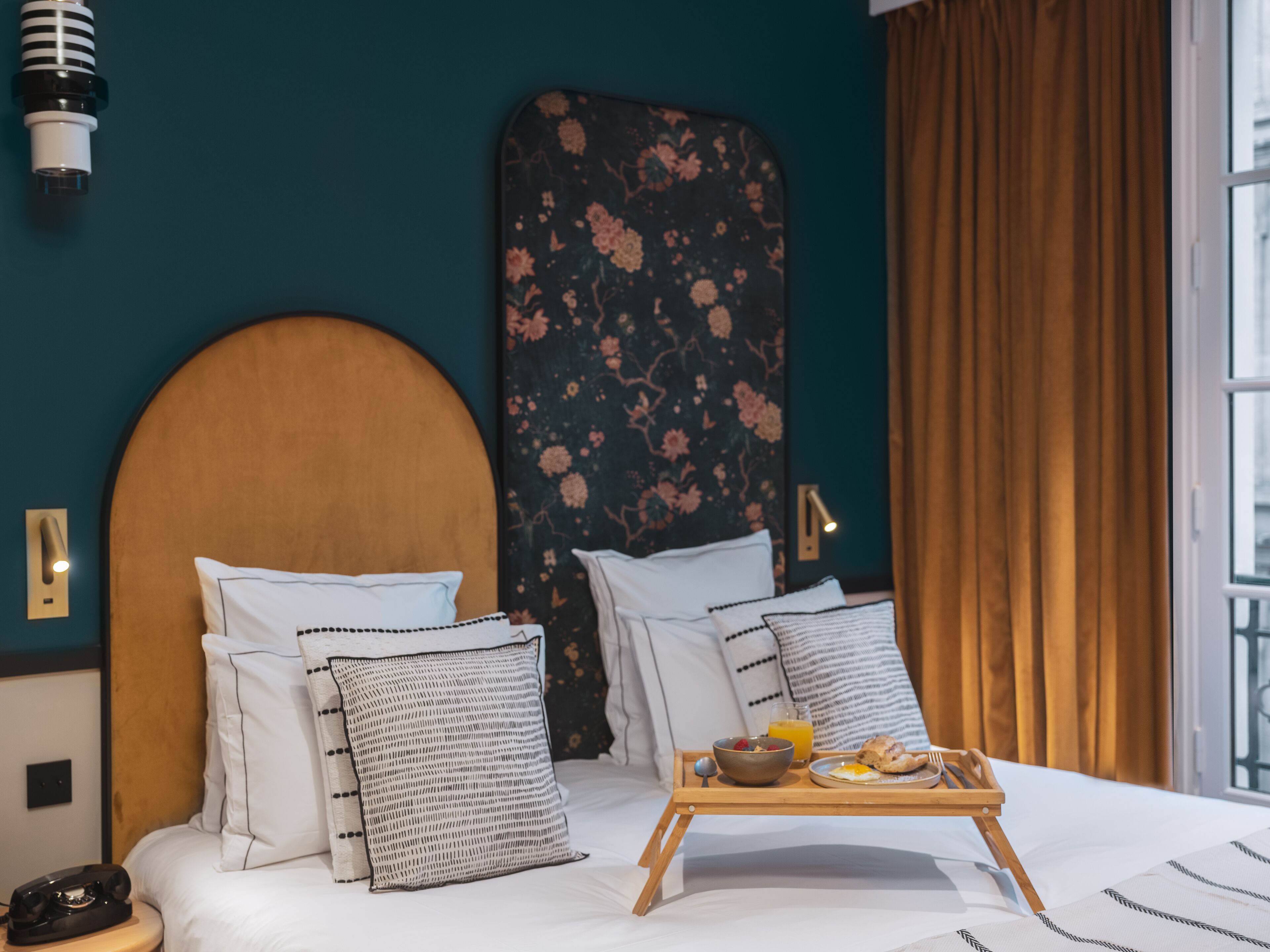 Camera d'albergo con un letto, cuscini, un vassoio con prodotti per la colazione, un telefono e un punto luce a parete.